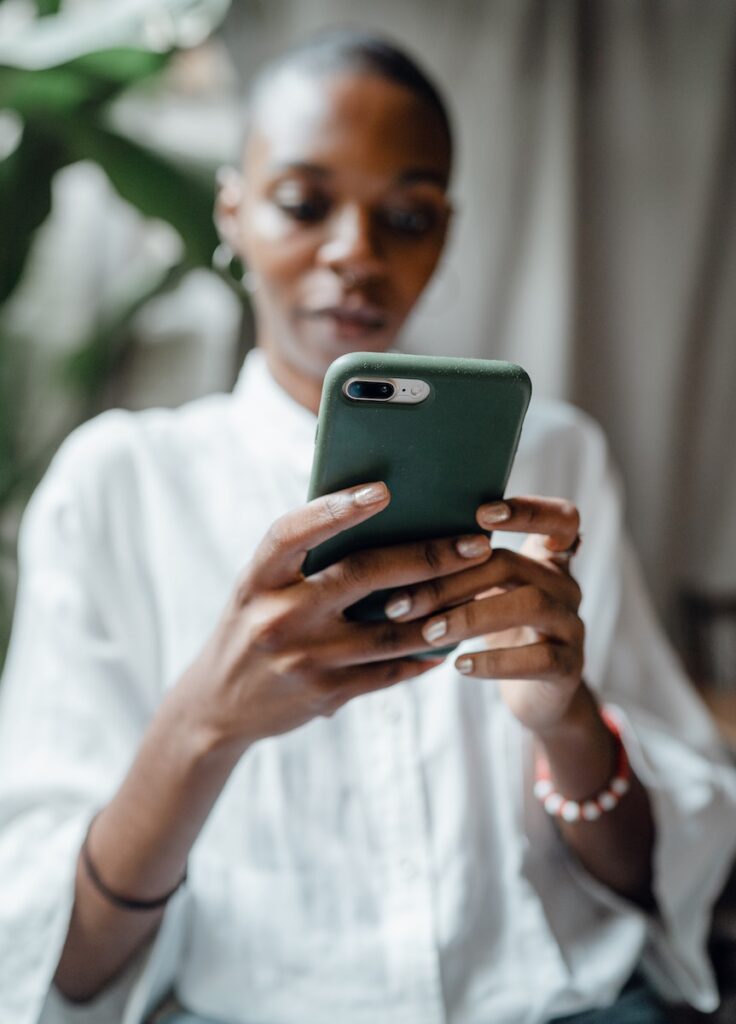 Schwarze Frau, die auf einem modernen Mobiltelefon Nachrichten schreibt